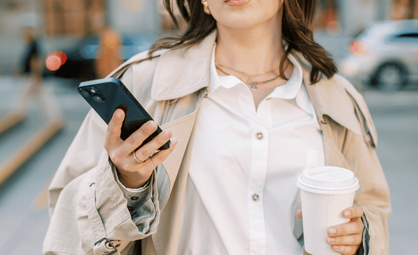 woman walking with a coffee and looking at her phone
